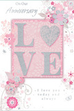 This anniversary card captures the feeling of quiet, enduring romance, like sharing a slow evening together after flowers have been delivered to a Brixton home. At the centre, the word LOVE appears in softly raised glitter, its letters edged with a fine sparkle that shifts between pastel pink and cool silver. The O is subtly suggested as a heart shape within the lettering, giving the design a gentle, affectionate focus. This central motif rests on a smooth, blush-pink background that glows with a powdery softness, setting a serene, intimate tone. Around it, delicate illustrated blooms in shades of blush, mauve, and soft white seem to unfurl in gentle arcs, their petals drawn with an almost watercolour lightness. Fine lines and airy shading echo the fluid shapes of spring garden flowers you might spot in nearby Brockwell Park, adding a sense of natural movement. Threaded between the blossoms are tiny flourishes: swirling tendrils, scattered petals, and the faint suggestion of butterflies drifting through the design, all contributing to a feeling of whimsical grace. Above and below the central motif, understated script phrases such as On Our Anniversary and I love you today and always are penned in a calm, flowing hand, mirroring the easy rhythm of a long, shared relationship. The card's colour story-soft pastel pinks balanced with silvery greys-feels soothing and timeless. Overall, the composition reads like a whispered promise, a paper memento that pairs beautifully with a romantic bouquet delivered across Brixton to mark another year of love.